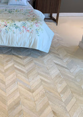 A cowhide patchwork rug with a geometric pattern in a champagne color, laid out on a floor next to a bed with a floral-patterned blanket.